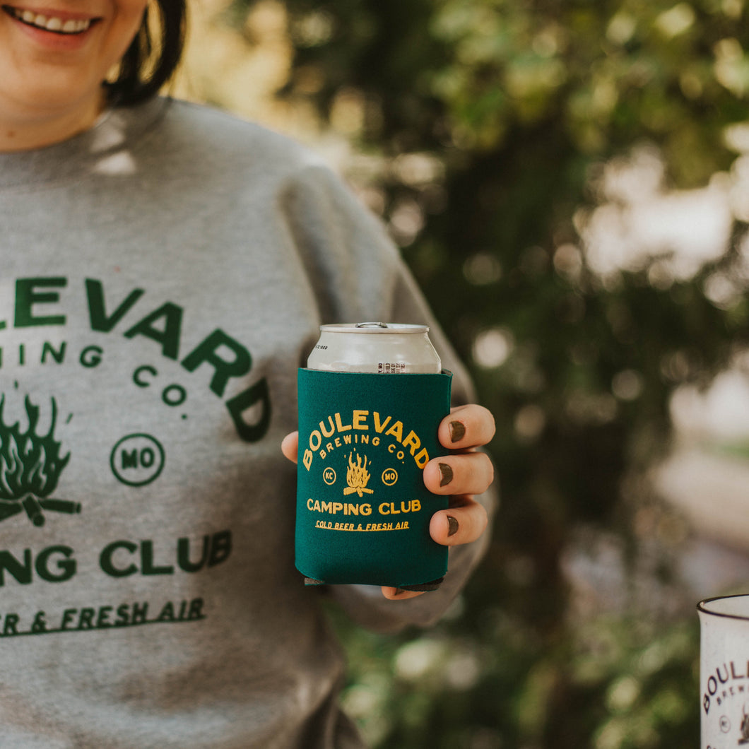 A woman holding a beer with the Camping Club Koolie on it.