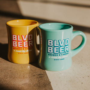 A yellow mug and teal mug next to each other that say  BLVD BEER