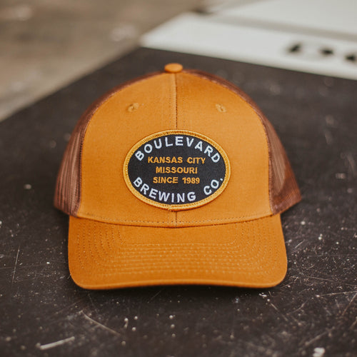 A brown trucker cap with a circular patch on the ground.