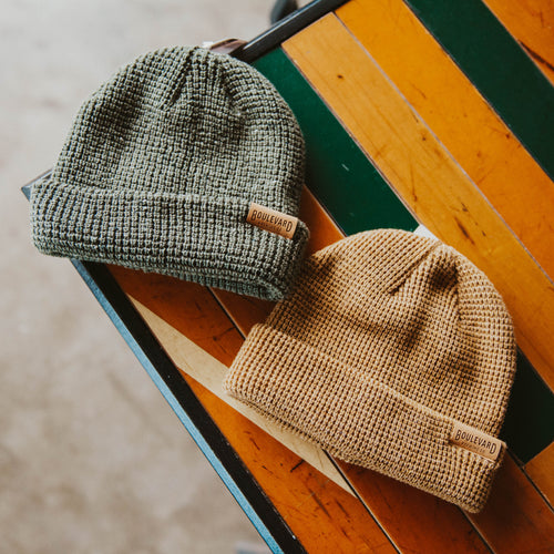 A green and khaki beanie, next to each other, on the table.