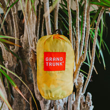 Load image into Gallery viewer, A packed up hammock in a yellow pouch, against a tree.
